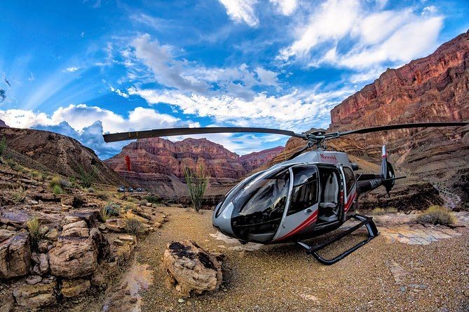 A helicopter landed in a rocky desert canyon under a vibrant blue sky with scattered clouds.