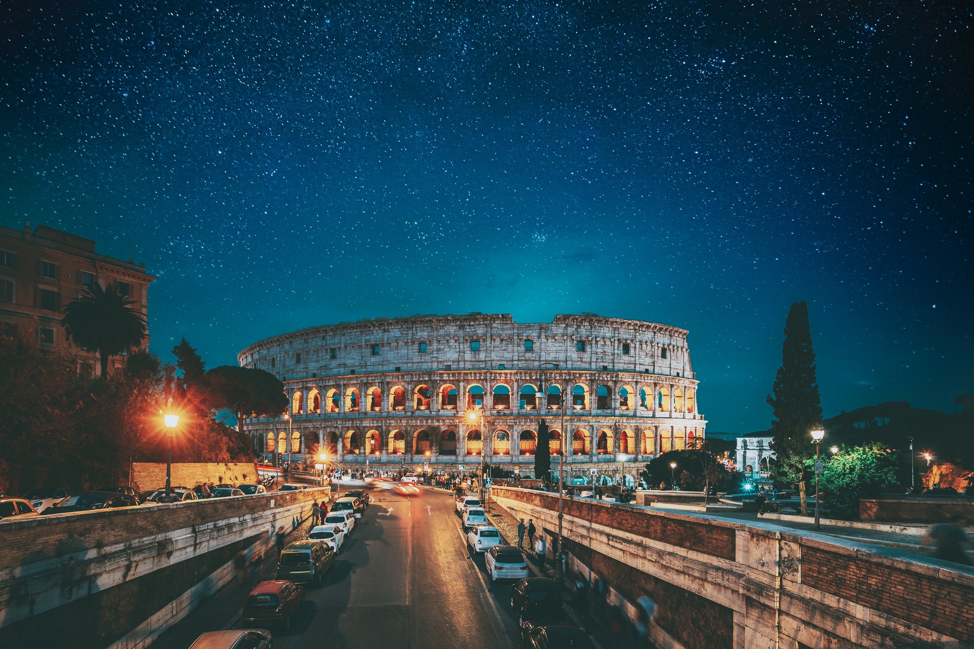 Rome, Italy. Bold Bright Blue Azure Night Starry Sky With Glowing Stars Above Colosseum Also Known As Flavian Amphitheatre In Evening Or Night Time. Travel To Italy